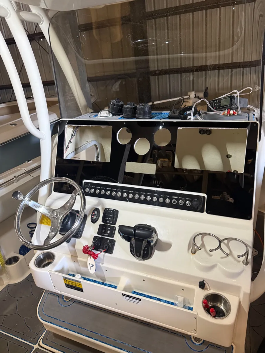 Panel negro montado en una consola de embarcación, con huecos para pantallas e instrumentos, una fila de interruptores y cableado accesible