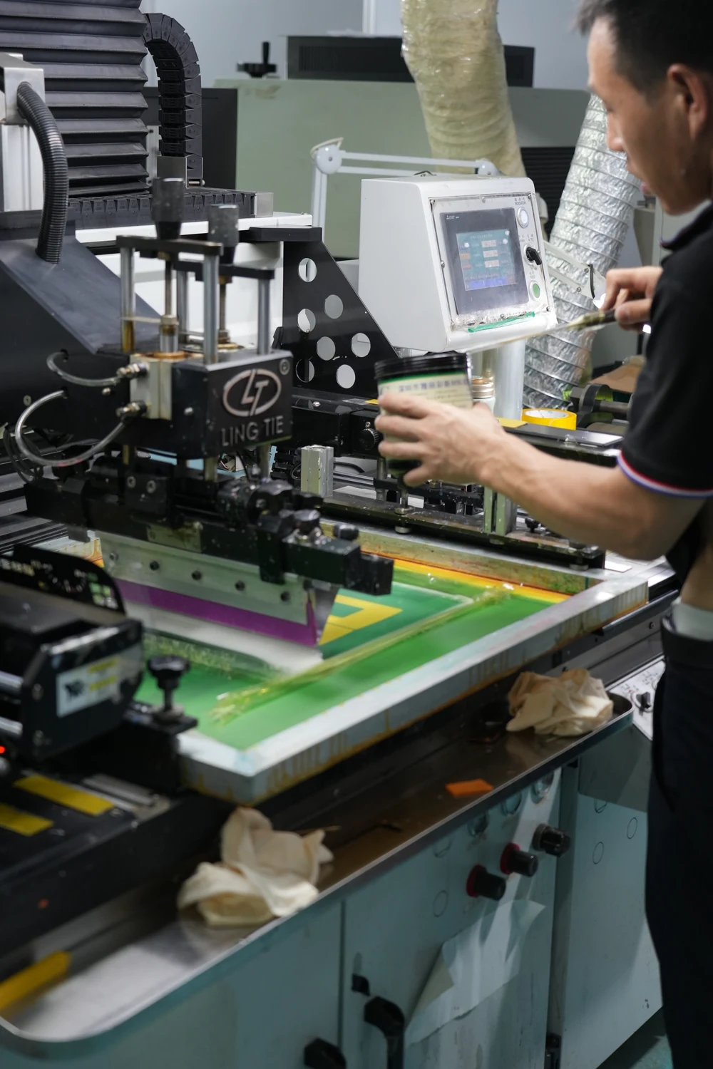 Operator working at screen-printing equipment with a squeegee and ink on a printing screen