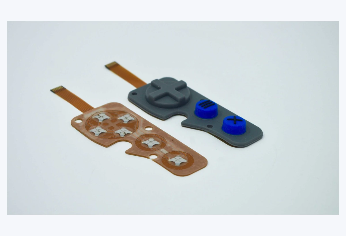 Gray and blue raised keypad buttons beside a flexible circuit with contact domes and tails