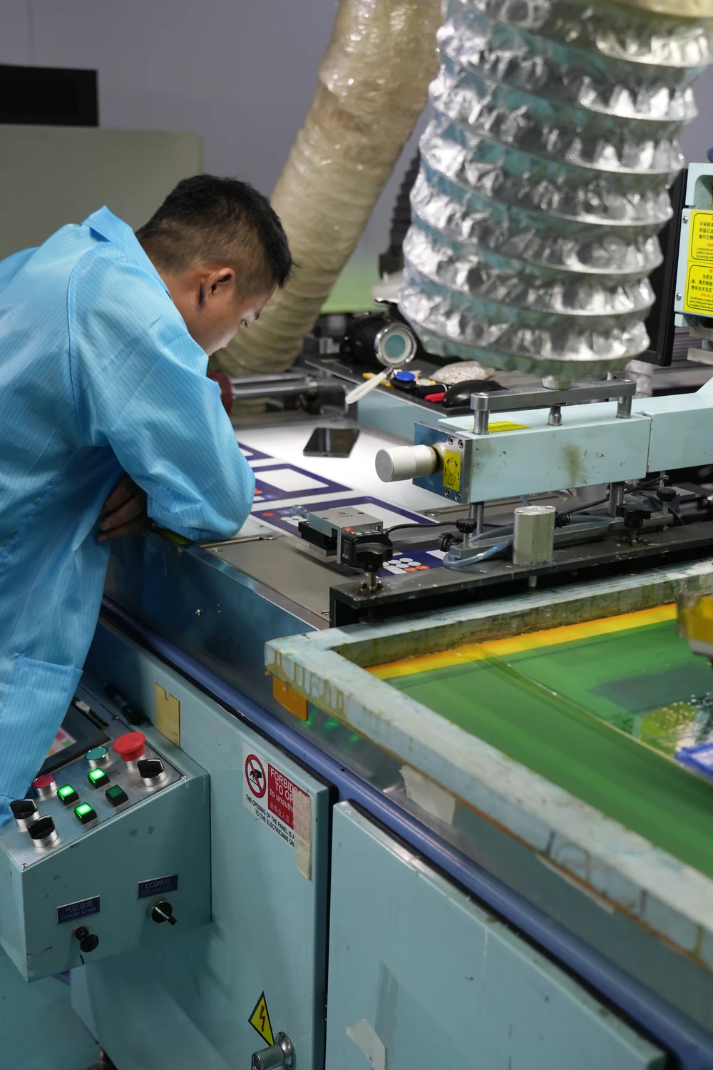 Factory operator positioning printed front-panel artwork at a screen-printing workstation