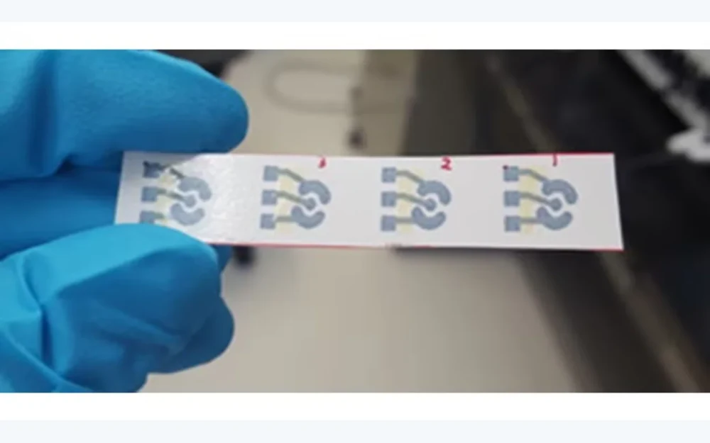 Gloved hand holding a strip of four printed electrochemical sensor patterns