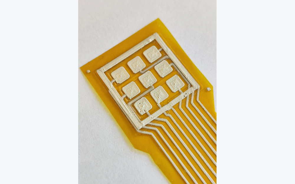 Primer plano de una matriz de electrodos impresos flexible con pistas de plata y nueve zonas de contacto