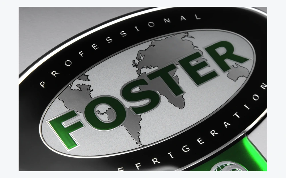 Nahaufnahme eines FOSTER-Dominglabels auf einer Metalloberfläche mit reflektierendem gewölbtem Rand