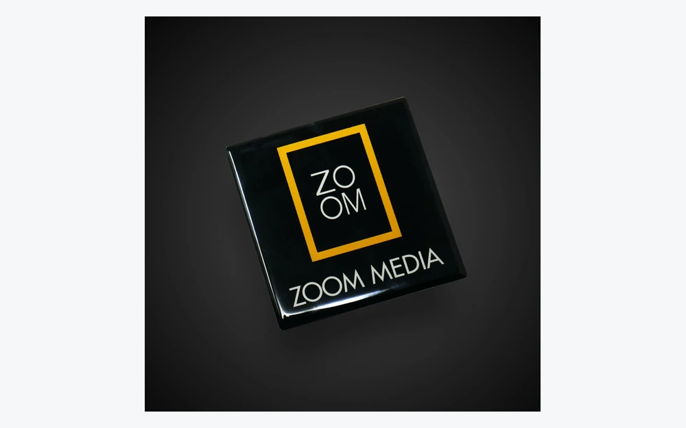 Schräg fotografiertes schwarzes ZOOM-MEDIA-Harzlabel mit glänzender Oberfläche und erhöhtem transparentem Rand